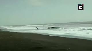 A car gets stuck in sand and is lashed by waves, at a beach in Palgarh